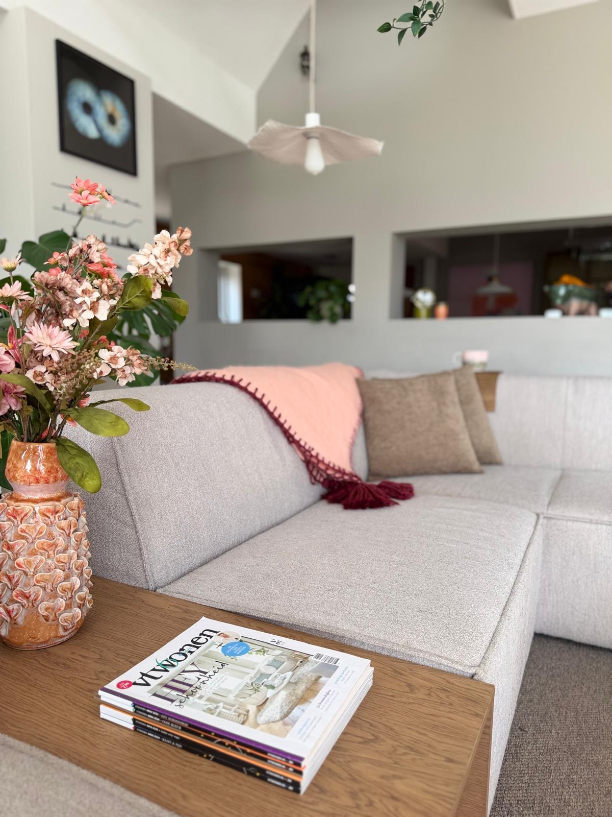 Woonkamer met bouclé bank, bloemen en interieurmagazines